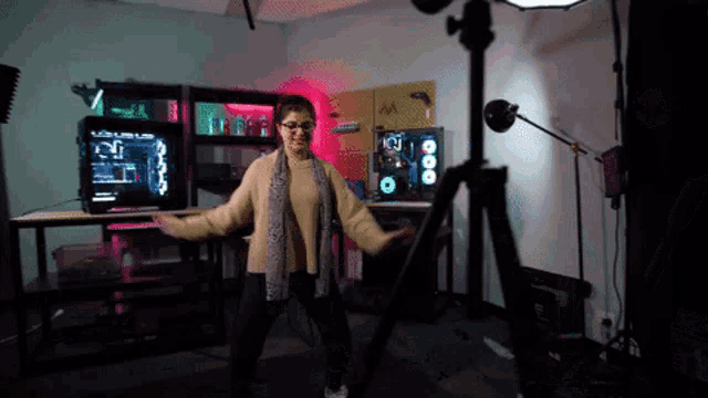 a woman is dancing in front of a camera in a room with a computer in the background