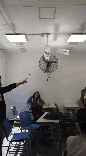 a man pointing at a ceiling fan in a classroom with students