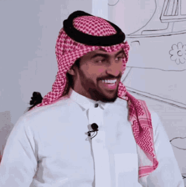 a man wearing a white shirt and a pink and black head scarf smiles