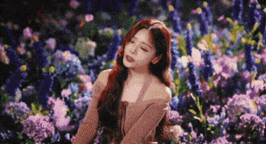 a woman is sitting in a field of purple and blue flowers with her eyes closed .