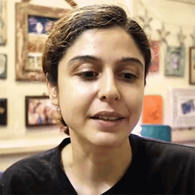 a close up of a woman 's face in front of a wall with pictures on it