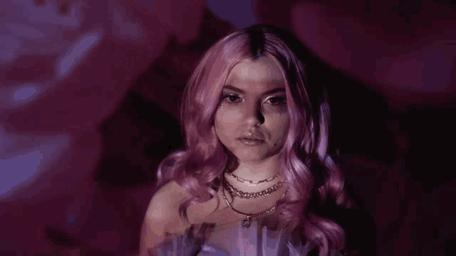 a woman with pink hair is wearing a necklace and a purple dress