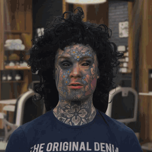 a man with tattoos on his face is wearing a blue shirt that says " feur "