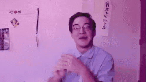 a man wearing glasses and a blue shirt is making a funny face while clapping his hands .