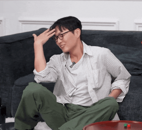 a man with glasses sits on a couch with his hand on his forehead