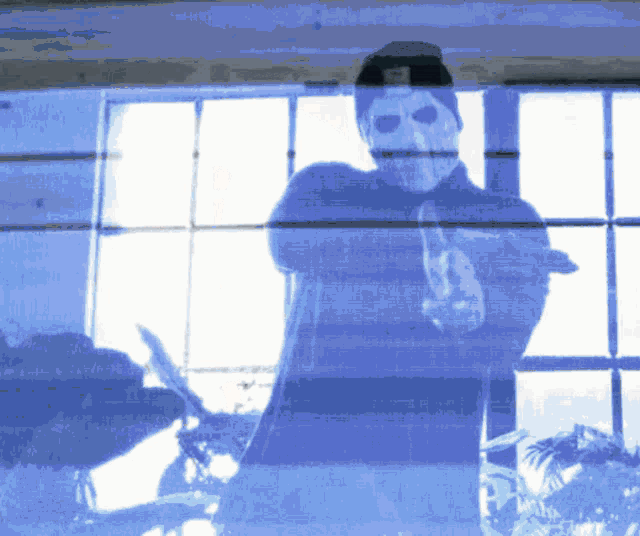 a man in a mask stands in front of a window with his arms crossed