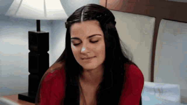 a woman with her eyes closed is sitting on a bed next to a lamp