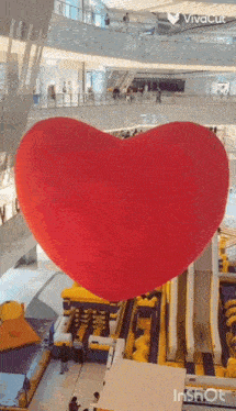 a large red heart shaped balloon is hanging from the ceiling of a mall