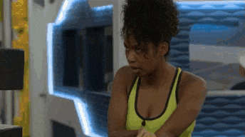 a woman in a yellow tank top is standing in a room with her arms crossed and looking at the camera .