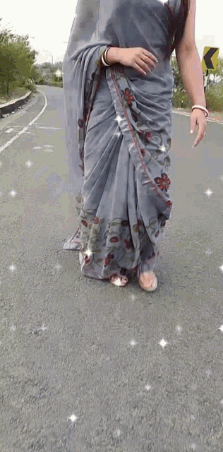 a woman wearing a gray floral saree is walking down the road .