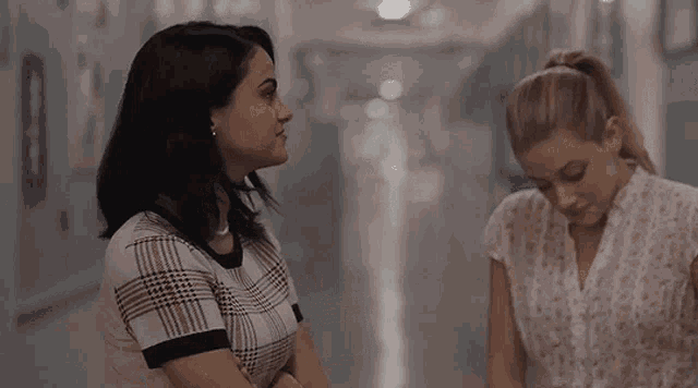 a woman in a plaid shirt is standing next to another woman in a white shirt in a hallway .