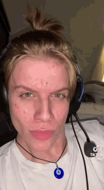 a man wearing headphones and a tik tok necklace looks at the camera