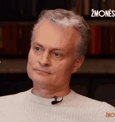 a man in a white sweater has a microphone around his neck and the word zmones is on the bottom right