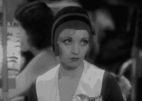 a black and white photo of a woman in a hat looking at the camera .