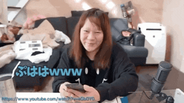 a woman is sitting in front of a microphone holding a cell phone and smiling while a url is displayed below her
