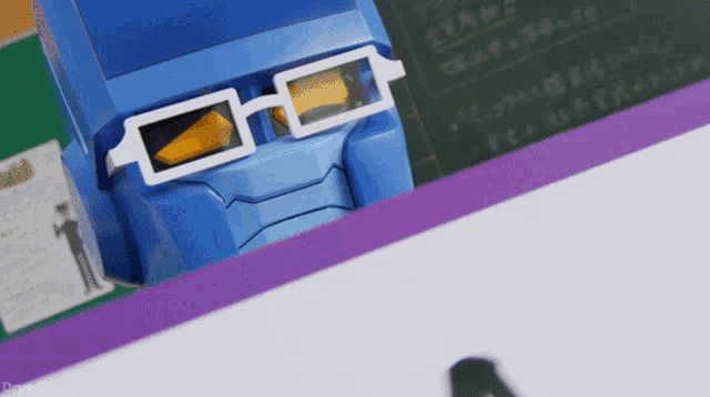 a blue robot wearing white glasses sits on a desk