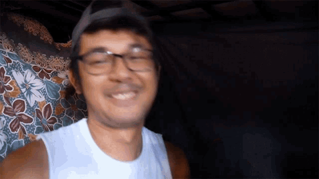 a man wearing glasses and a hat is smiling in front of a floral curtain