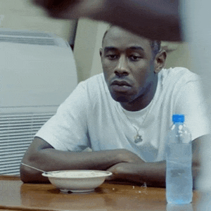 a man in a white shirt sits at a table with a bowl of food and a bottle of water