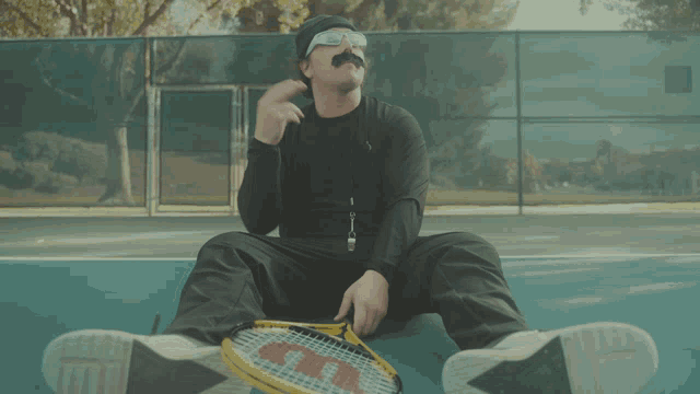a man with a mustache is sitting on a tennis court with a wilson tennis racquet
