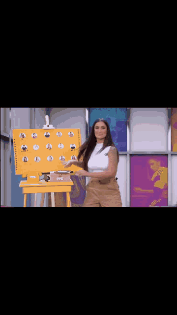 a woman is standing in front of an easel with a board with pictures of people on it ..