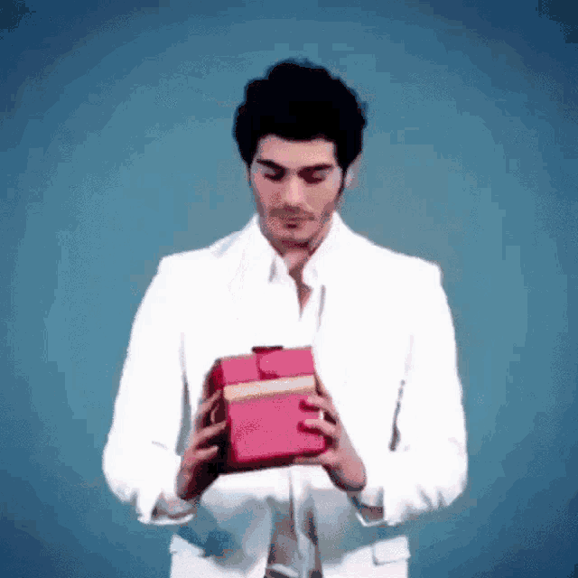 a man in a white suit is holding a red box in his hands .