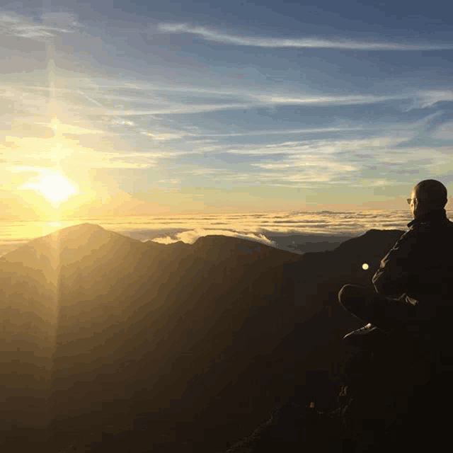 a person sitting on top of a mountain watching the sun set