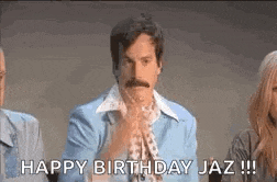 a man with a mustache is sitting in front of a group of people and saying happy birthday jaz .