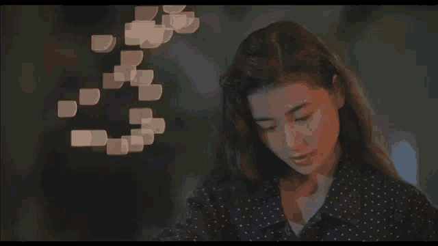 a woman in a polka dot shirt is looking at the camera with a blurry background of lights behind her .