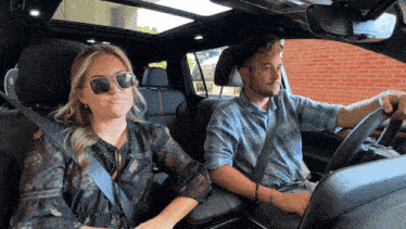 a man and a woman are sitting in a car with the woman wearing sunglasses