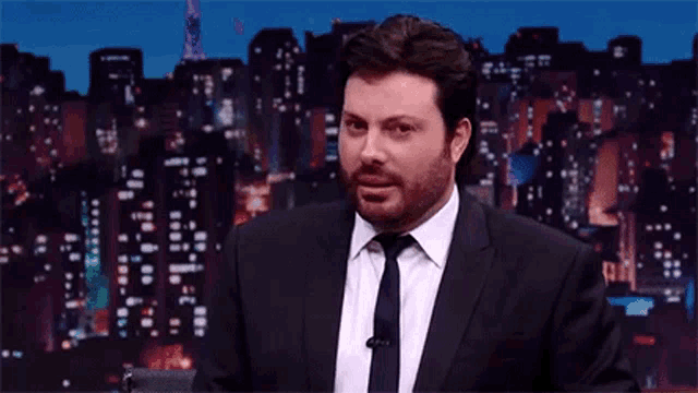 a man in a suit and tie is making a funny face in front of a city skyline .
