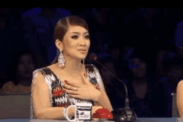 a woman sitting in front of a microphone with her hand on her chest holding a mug that says ' a ' on it