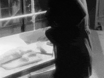 a black and white photo of a woman standing in front of a glass display case .