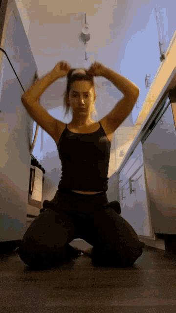 a woman in a black tank top is kneeling on the floor