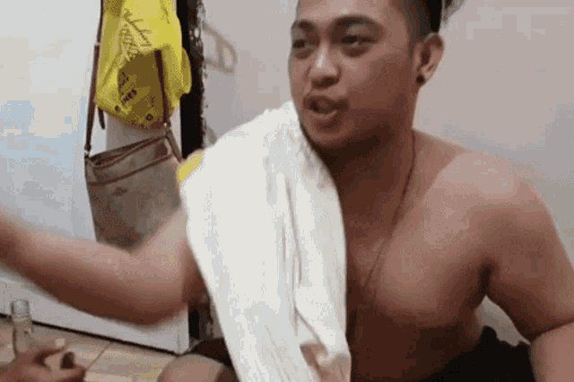 a man without a shirt is sitting on the floor with a towel around his neck .