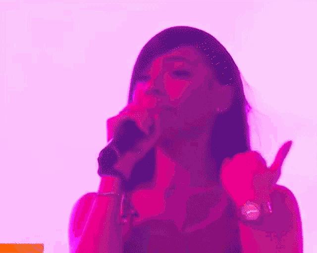a woman is singing into a microphone in front of a pink background