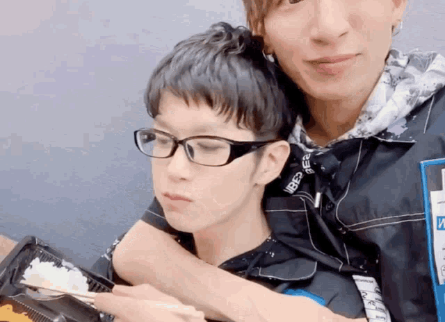 a man wearing glasses is hugging another man who is holding a container of food