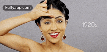 a woman wearing red lipstick and earrings is smiling and pointing her finger at her forehead ..
