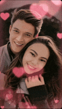 a man and a woman are posing for a picture with pink hearts surrounding them