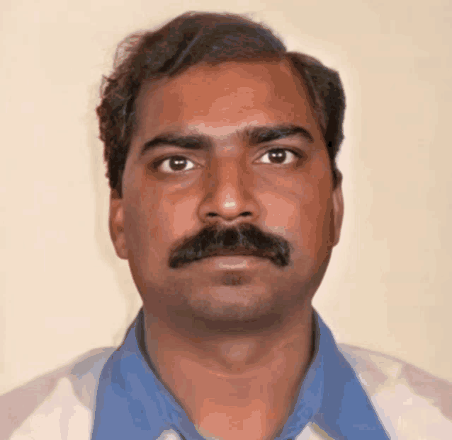a man with a mustache looks at the camera