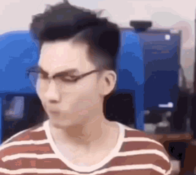 a man wearing glasses and a striped shirt is sitting in front of a blue machine .