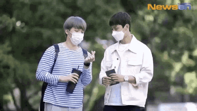 a couple of men wearing face masks are standing next to each other in a park .