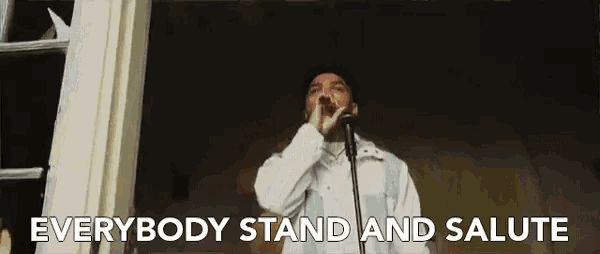a man is singing into a microphone with the words `` everybody stand and salute '' above him .