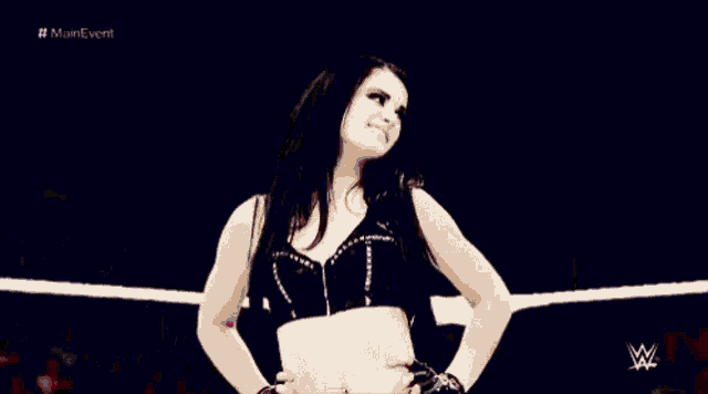 a female wrestler is standing in a ring with her hands on her hips .