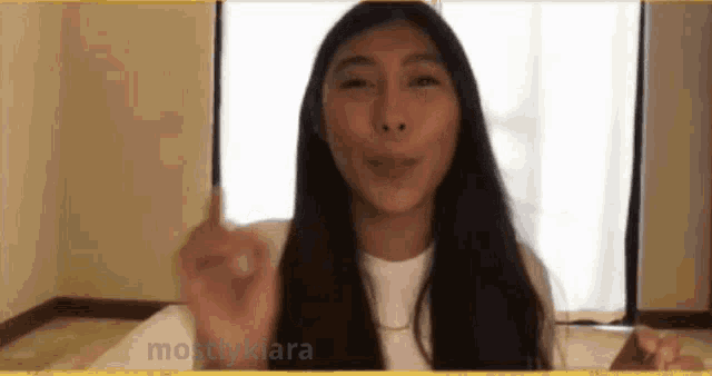 a woman with long hair is making a funny face and pointing at the camera .