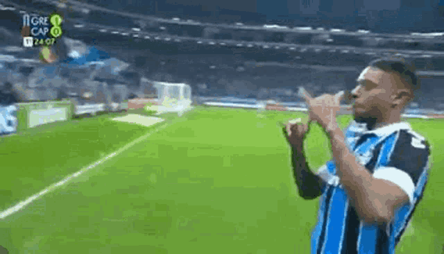 a man is standing on a soccer field making a peace sign .