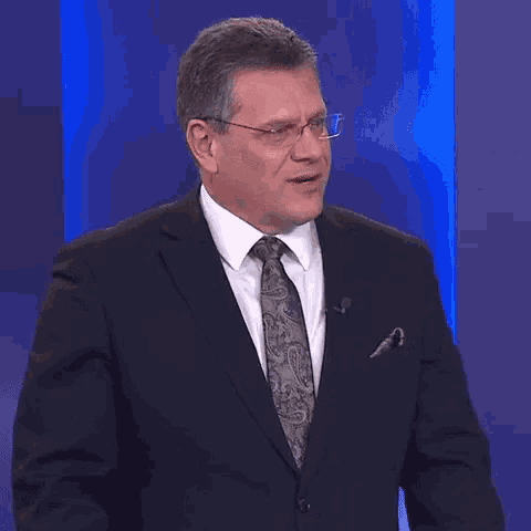 a man in a suit and tie is smiling in front of a blue wall