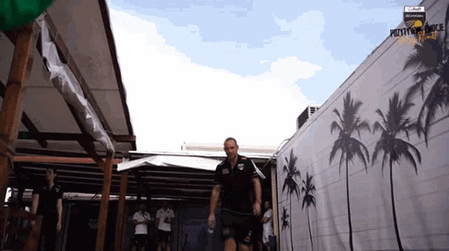 a man walking in front of a building with palm trees painted on the wall
