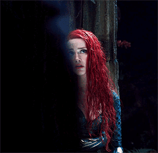 a woman with red hair and a blue dress is standing next to a pillar