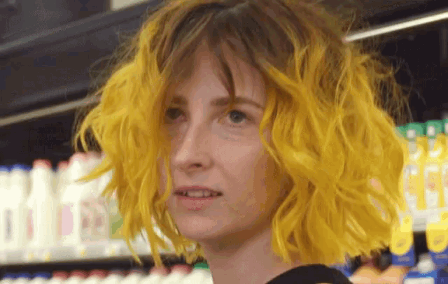 a woman with bright yellow hair is standing in front of a shelf of milk