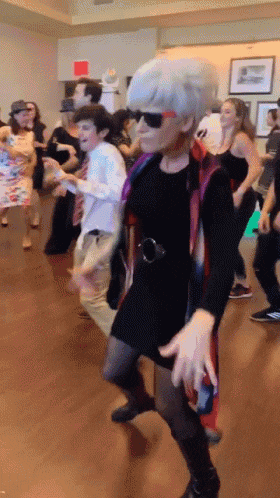 a group of people are dancing in a room with a red exit sign in the background